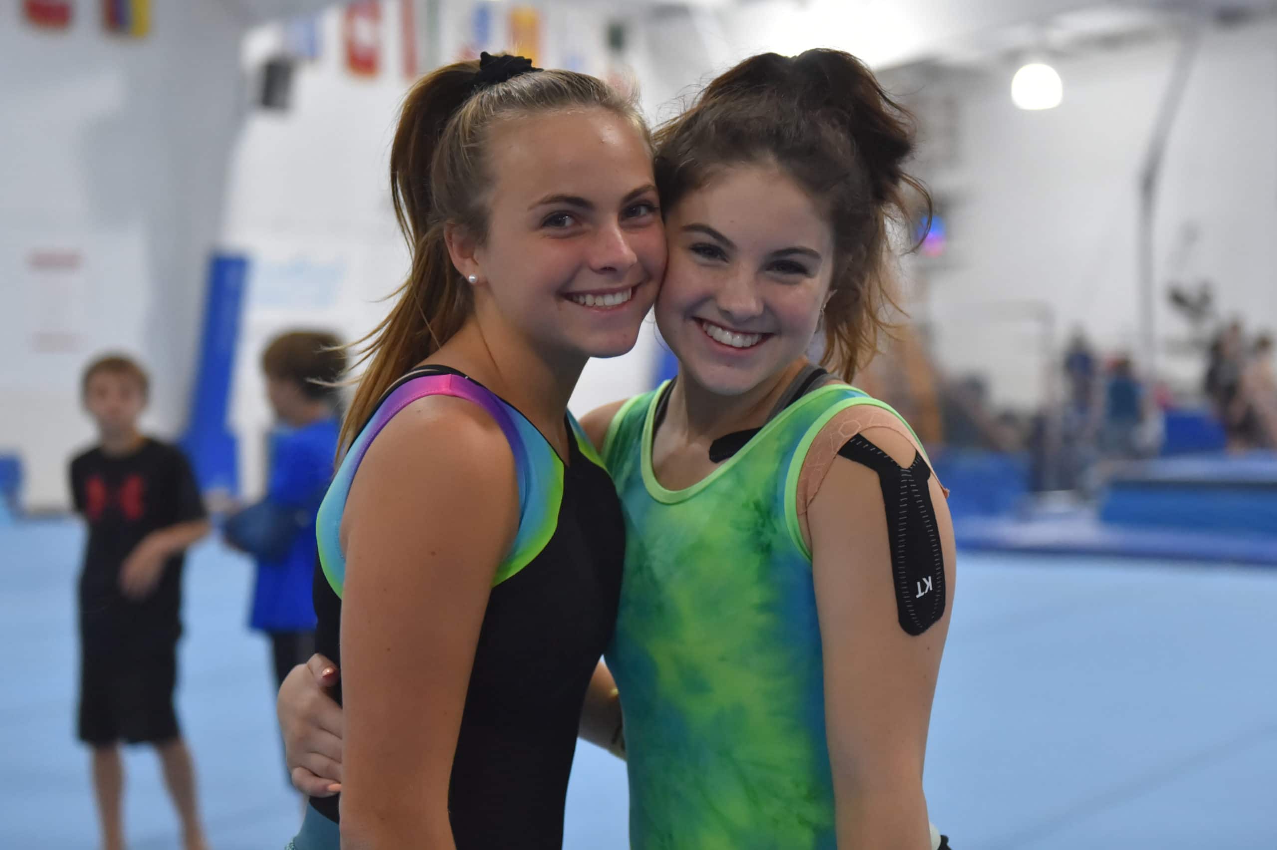 Two girl campers pose for a photo together. One camper has athletic tape on her shoulder.