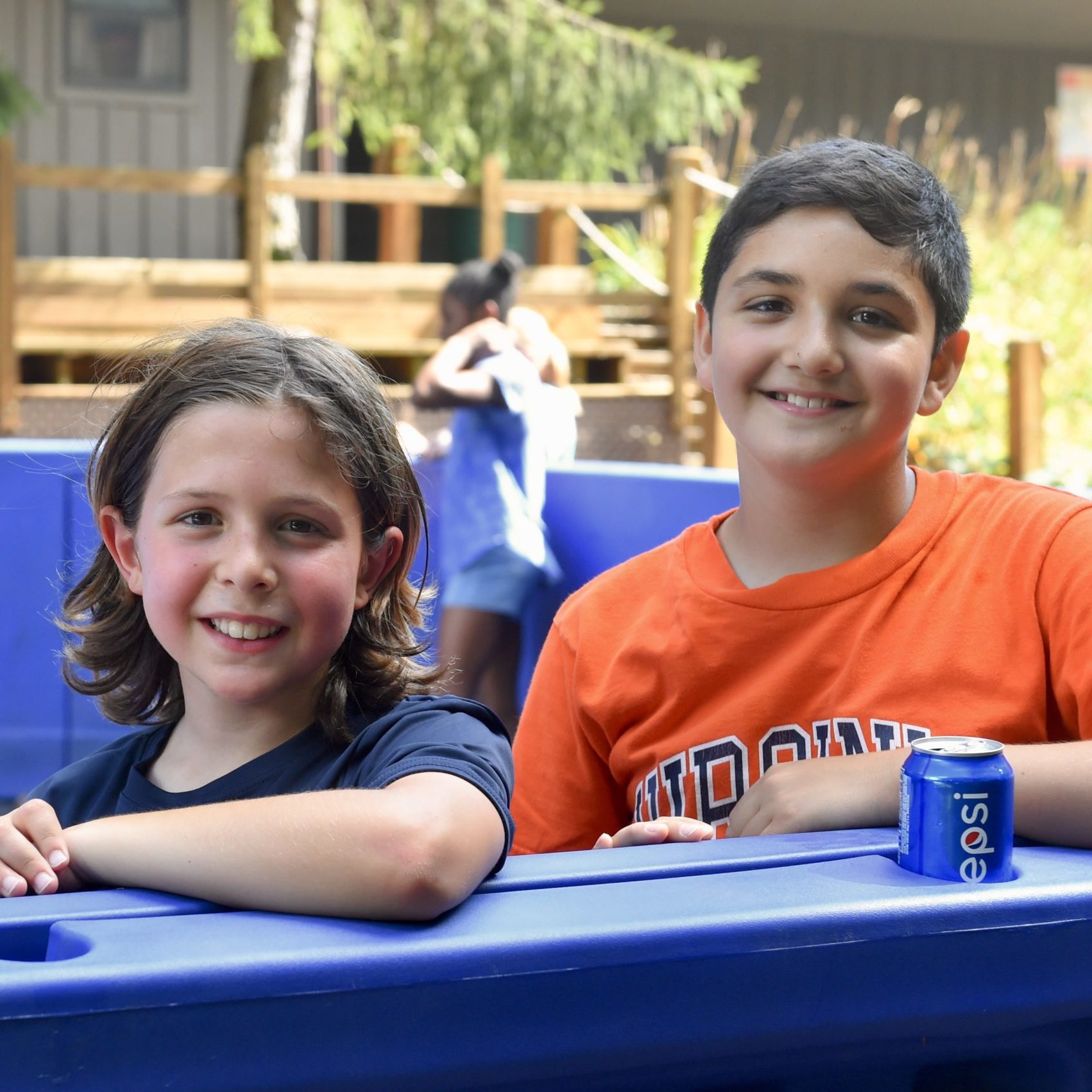 Two campers pose for a photo outside. One camper has a can of soda in front of him.