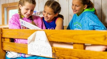 girls sitting atop one of the bunk beds in a cabin