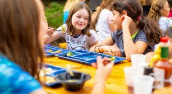 campers socializing while eating outside at picnic tables