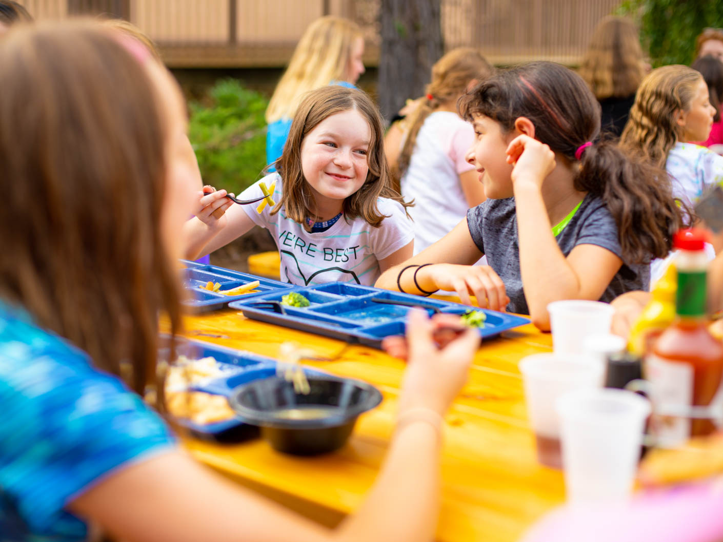 campers socializing while eating outside at picnic tables