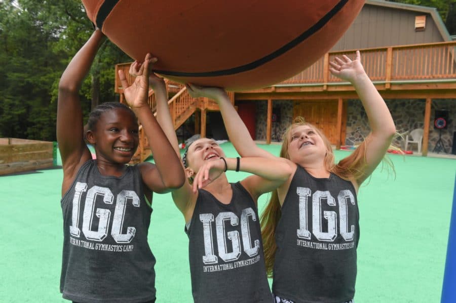 Three campers play with an oversized basketball while wearing IGC tank tops.