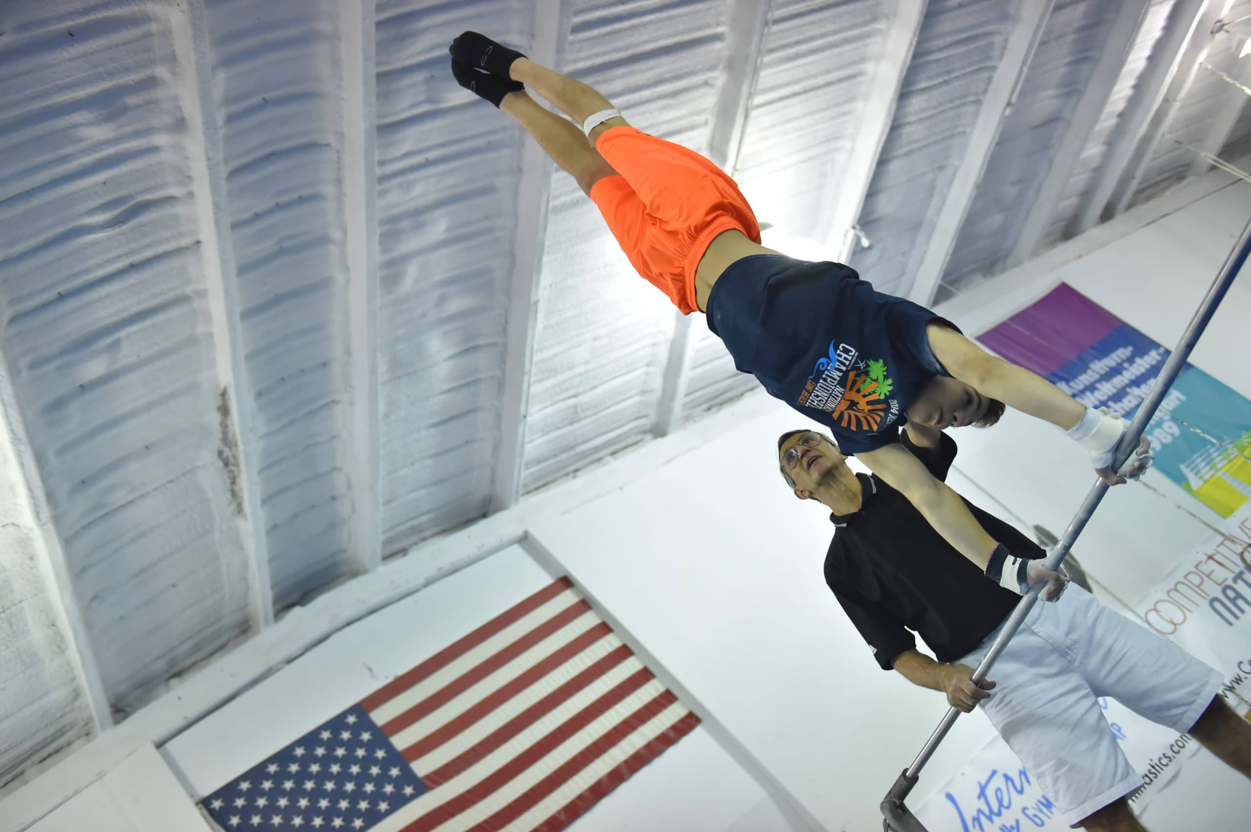A camper is upside down on bars as a coach watches.