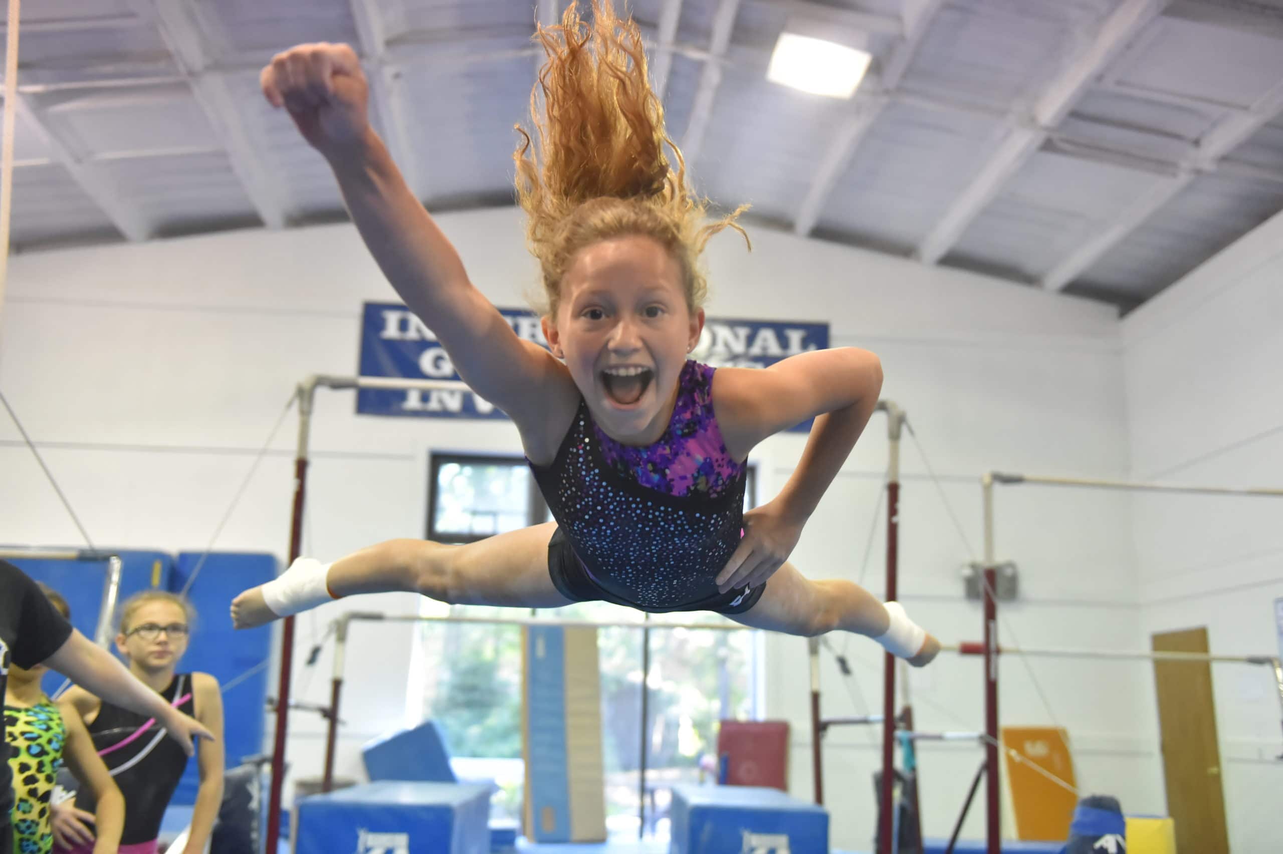 A camper poses and smiles for a photo mid air with her left arm extended outward.