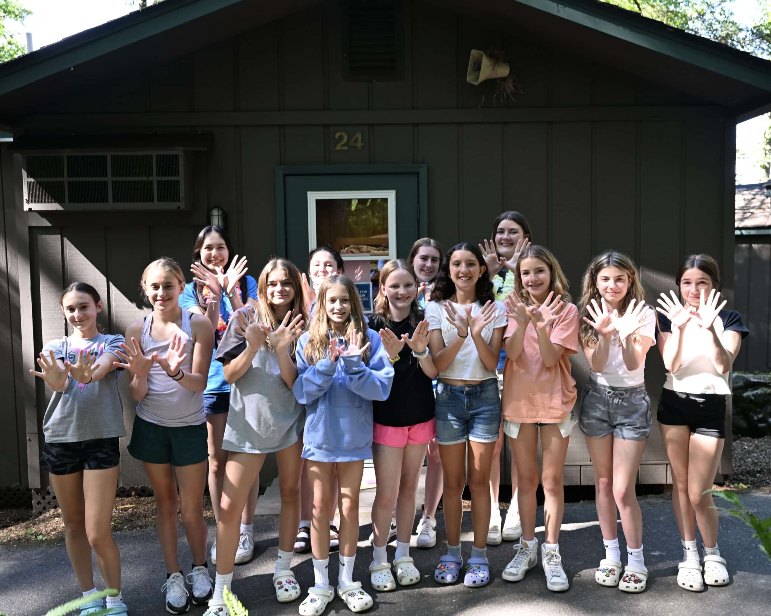 A group of campers pose for a photo standing in front of their cabin, while mimicking the Kount on Kindness logo