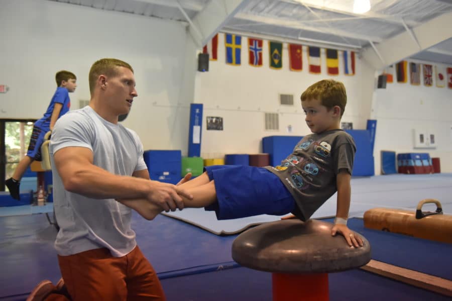 STEVE LEGENDRE assists a camper with a gymnastics move by holding onto his legs.
